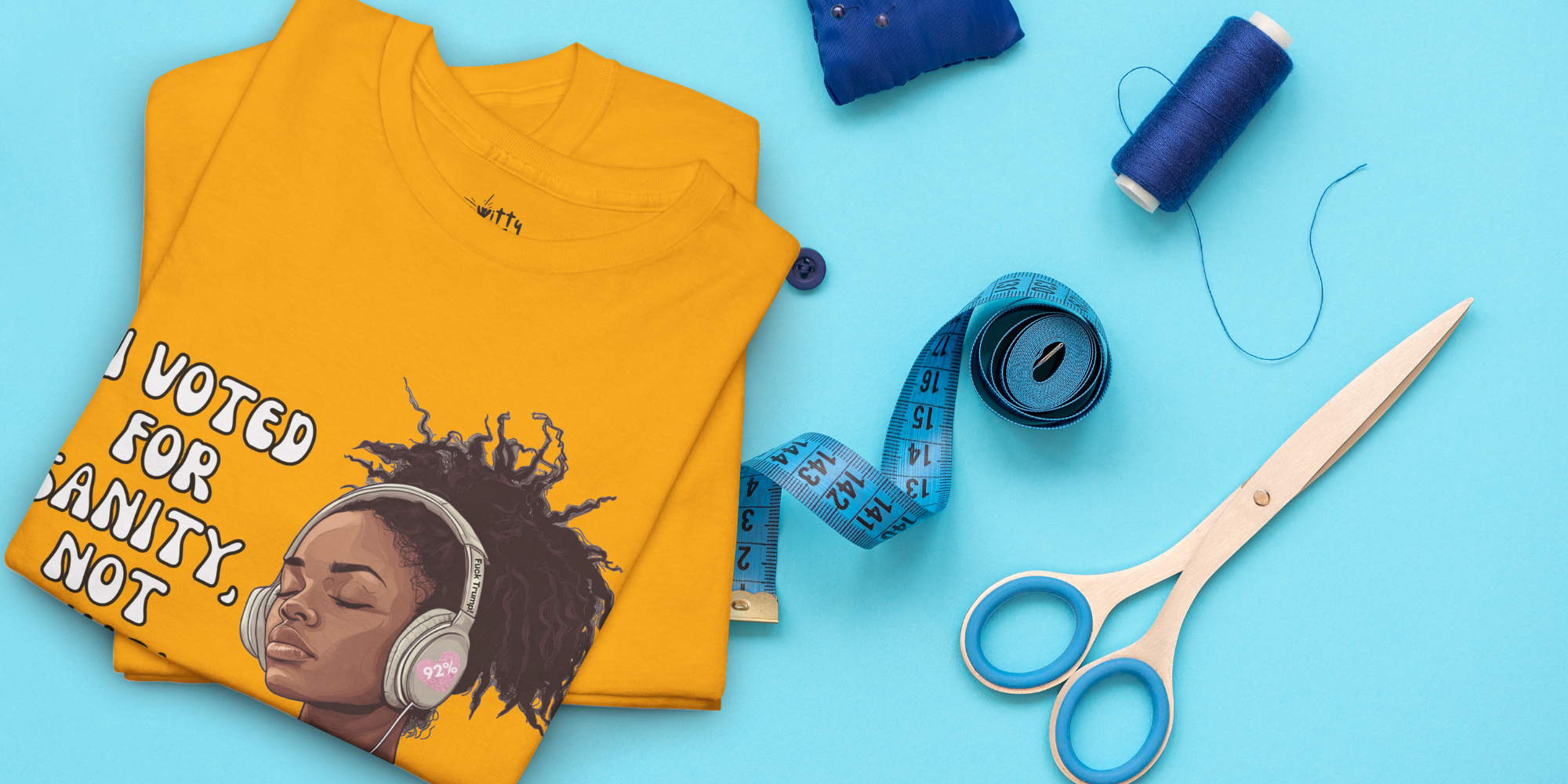 A folded yellow graphic T-shirt is laid flat on a bright blue background with sewing-themed props including blue thread spools, a measuring tape, and scissors. The shirt graphic shows a portrait of a woman with headphones and the text 'I VOTED FOR SANITY, NOT THIS'.