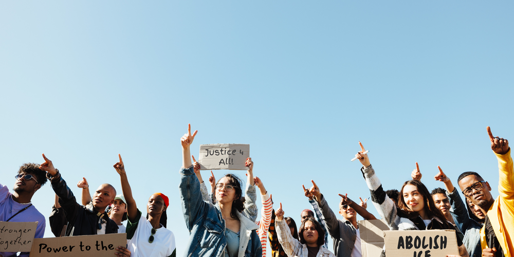 Group of people holding up signs with various messages against a clear blue sky.