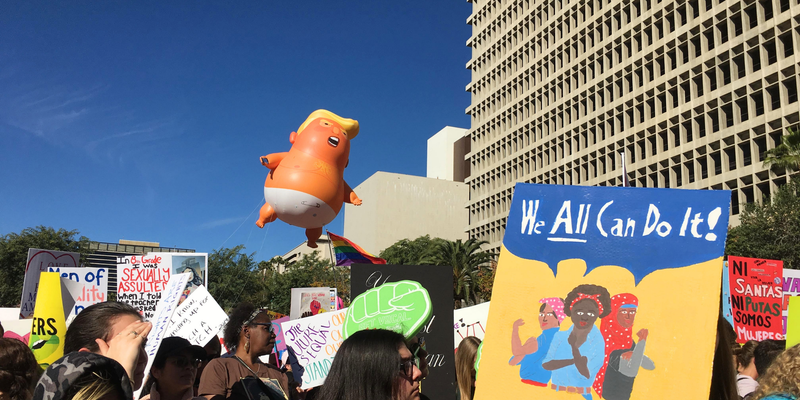 Protest scene with Toddler Trump balloon and signs in front of a building